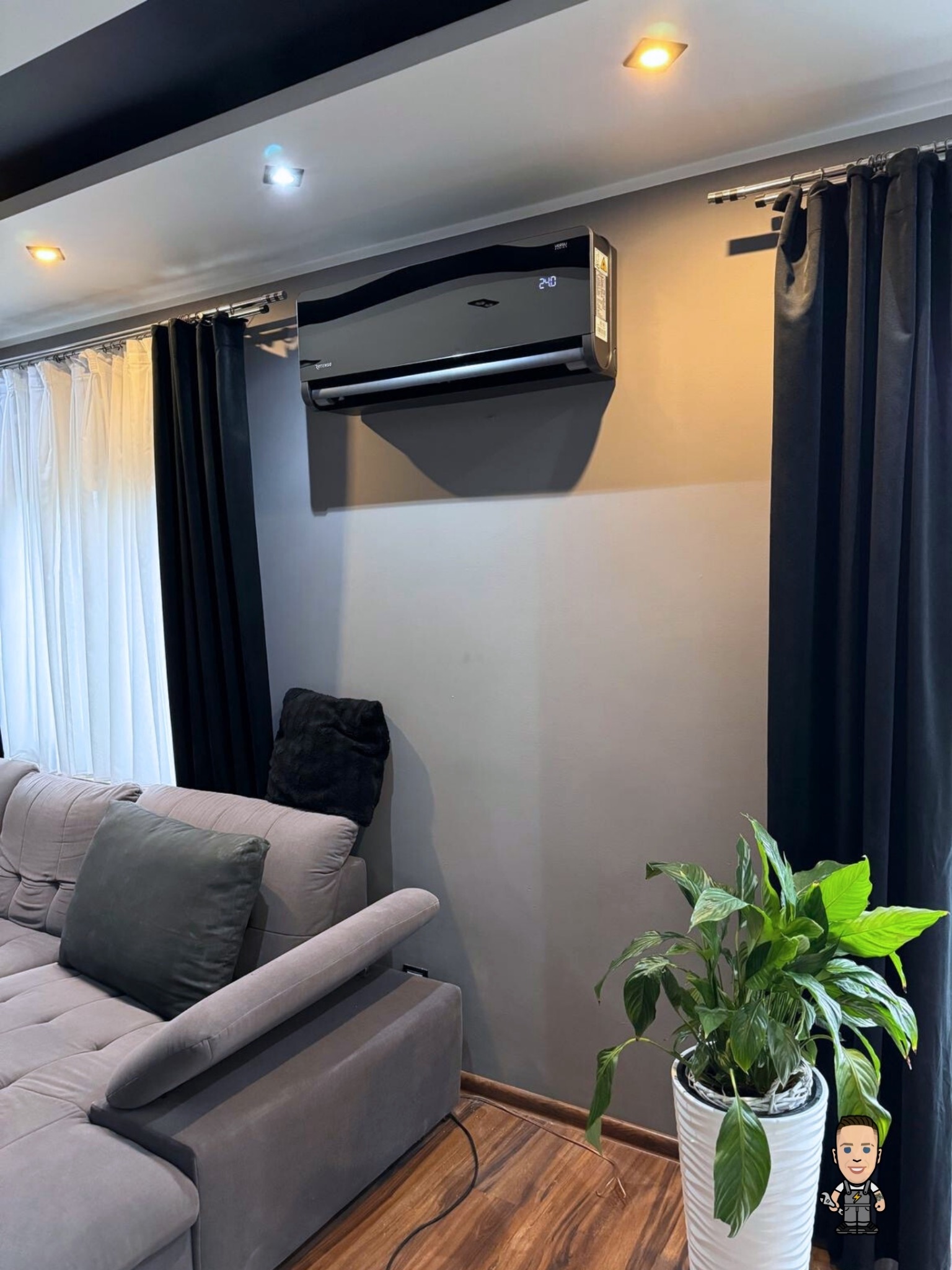 Czarny klimatyzator ścienny w nowoczesnym salonie w Bysławiu. Widoczne zasłony, sofa i roślina doniczkowa. Minimalistyczny design.