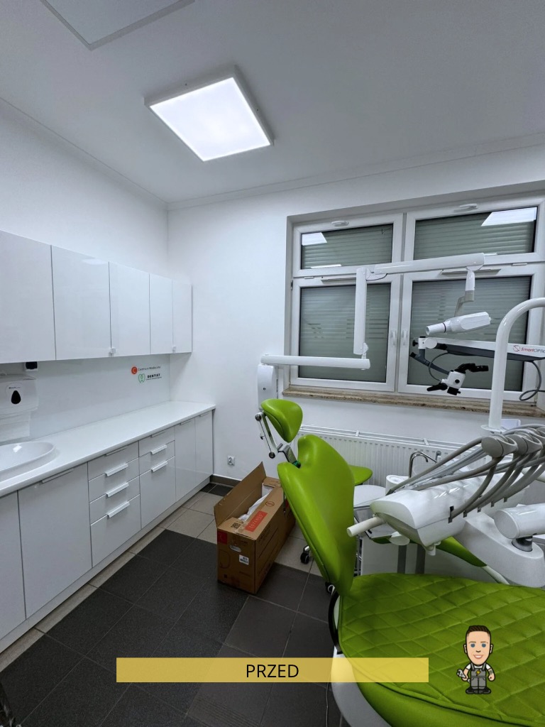 Wnętrze gabinetu dentystycznego przed montażem oświetlenia. Widoczny fotel dentystyczny, białe szafki i okno. Na podłodze leży karton.