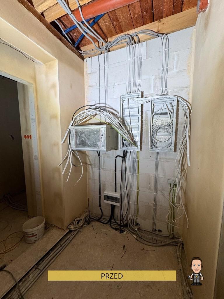 Rozbudowa instalacji elektrycznej w pomieszczeniu przed wykończeniem: widoczne kable, puszki i rozdzielnice na ścianie z bloczków. Etap prac w surowym stanie.