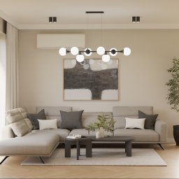 Proli Design Oliwia Pietras - Jasne wnętrze salonu z szarą sofą narożną, stolikami kawowymi i abstrakcyjnym obrazem na ścianie. Minimalistyczna lampa sufitowa i roślina doniczkowa dodają przytulności.