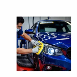 Pracownik w masce i rękawicach czyści reflektor niebieskiego samochodu żółtą ściereczką z mikrofibry. Widoczne detale karoserii i oświetlenie warsztatowe.