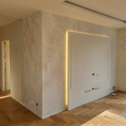 ADAMKO Tapetowanie Premium - Wykończone wnętrze: parkiet w jodełkę, ściana z efektem marmuru z podświetleniem LED, biała ściana z gniazdkami i otwarta przestrzeń. Nowoczesny design.