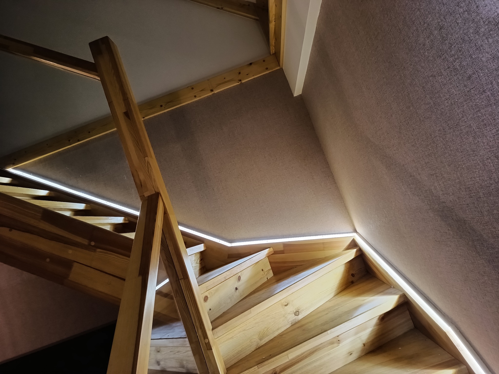 Drewniane schody z podświetleniem LED i tapetą na ścianie. Ujęcie z dołu, ukazujące detale wykończenia i nowoczesne oświetlenie.