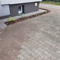 PPHU ARTEK ARTUR NOWAKOWSKI - Rabata z korą i roślinami ozdobnymi przy fundamencie budynku, obok wyłożony kostką brukową podjazd. Widok z góry, w tle zieleń.