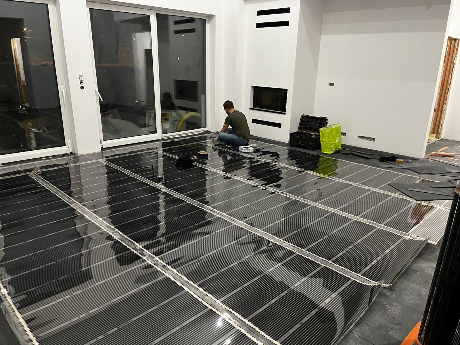 Montaż folii grzewczej na podłodze w nowoczesnym wnętrzu. Widoczny instalator w trakcie pracy, narzędzia i rozłożone panele grzewcze.