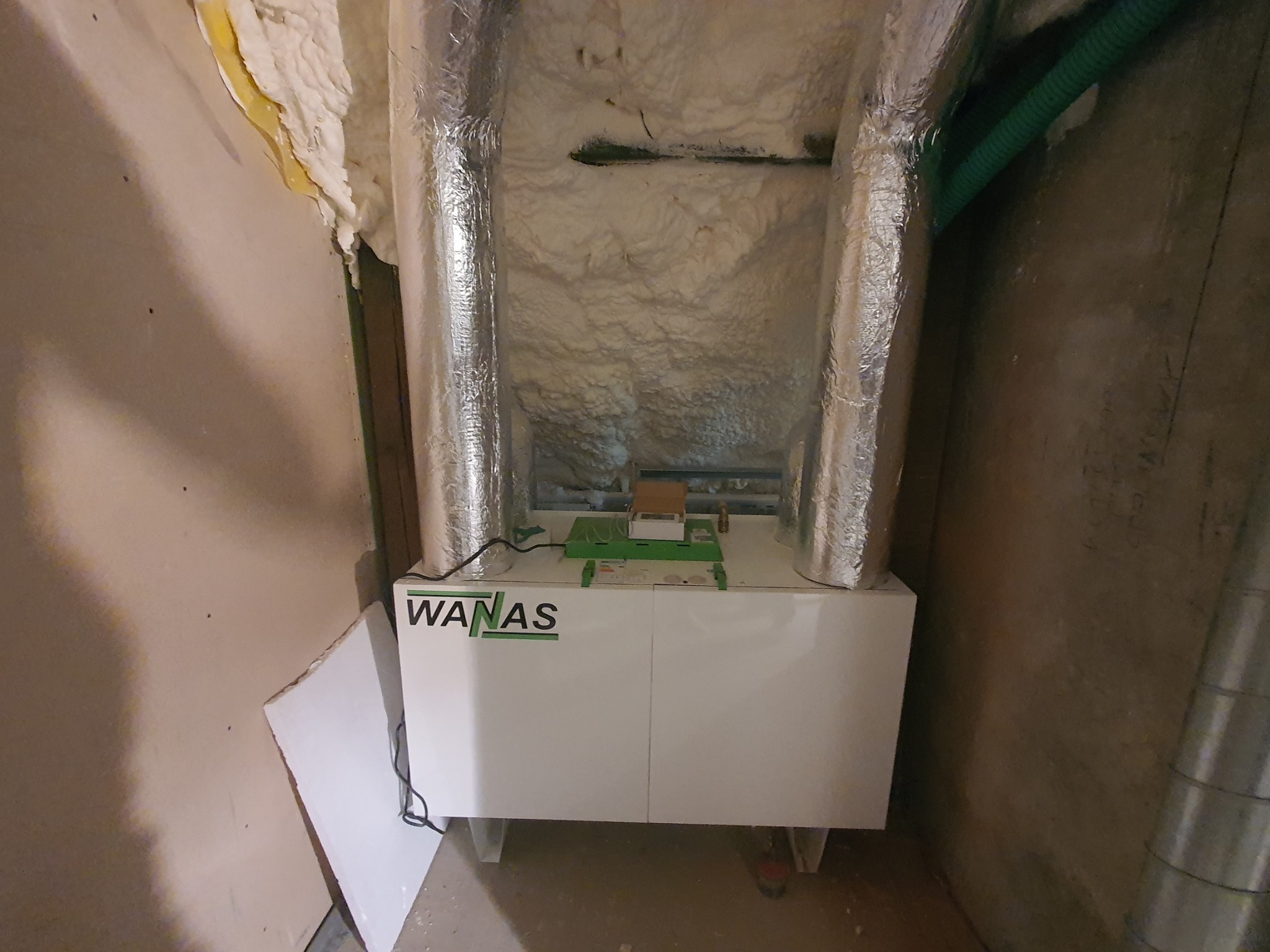 Centrala wentylacyjna WANAS z izolowanymi przewodami w surowym pomieszczeniu. Widoczne elementy instalacji i izolacja piankowa.
