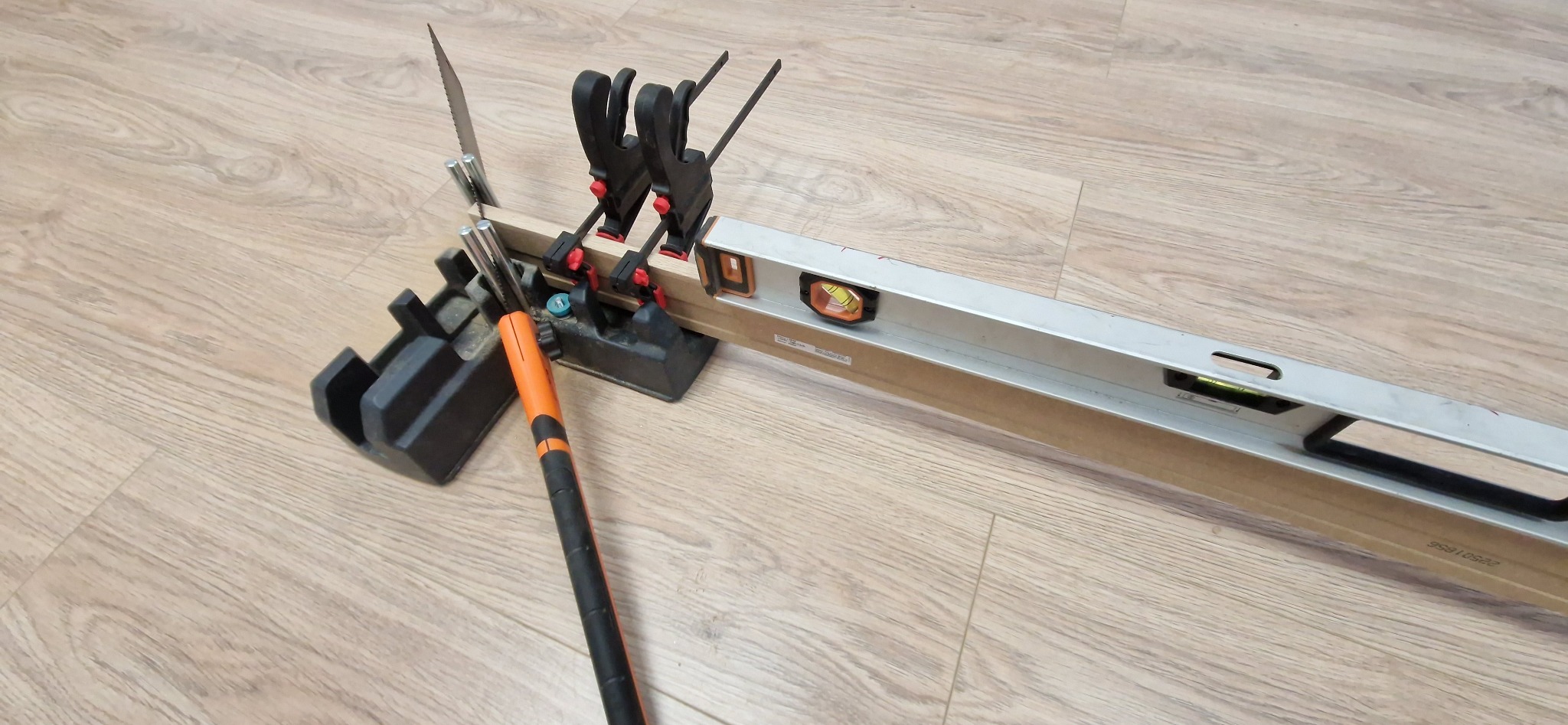 Przygotowanie do cięcia listwy przypodłogowej: piła w skrzynce uciosowej, poziomica i zaciski na drewnianej podłodze. Narzędzia gotowe do pracy.