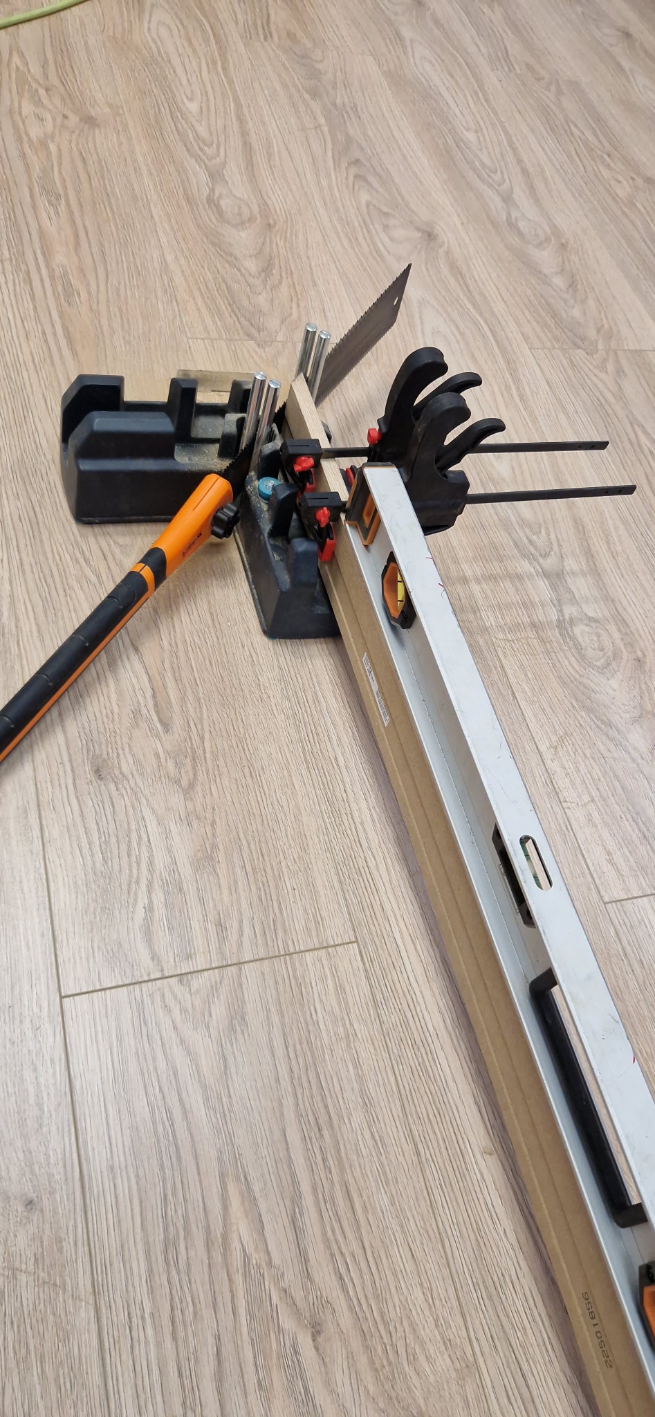 Przygotowanie do cięcia paneli podłogowych: piła ręczna w skrzynce uciosowej z poziomnicą na drewnianej podłodze. Narzędzia gotowe do pracy.