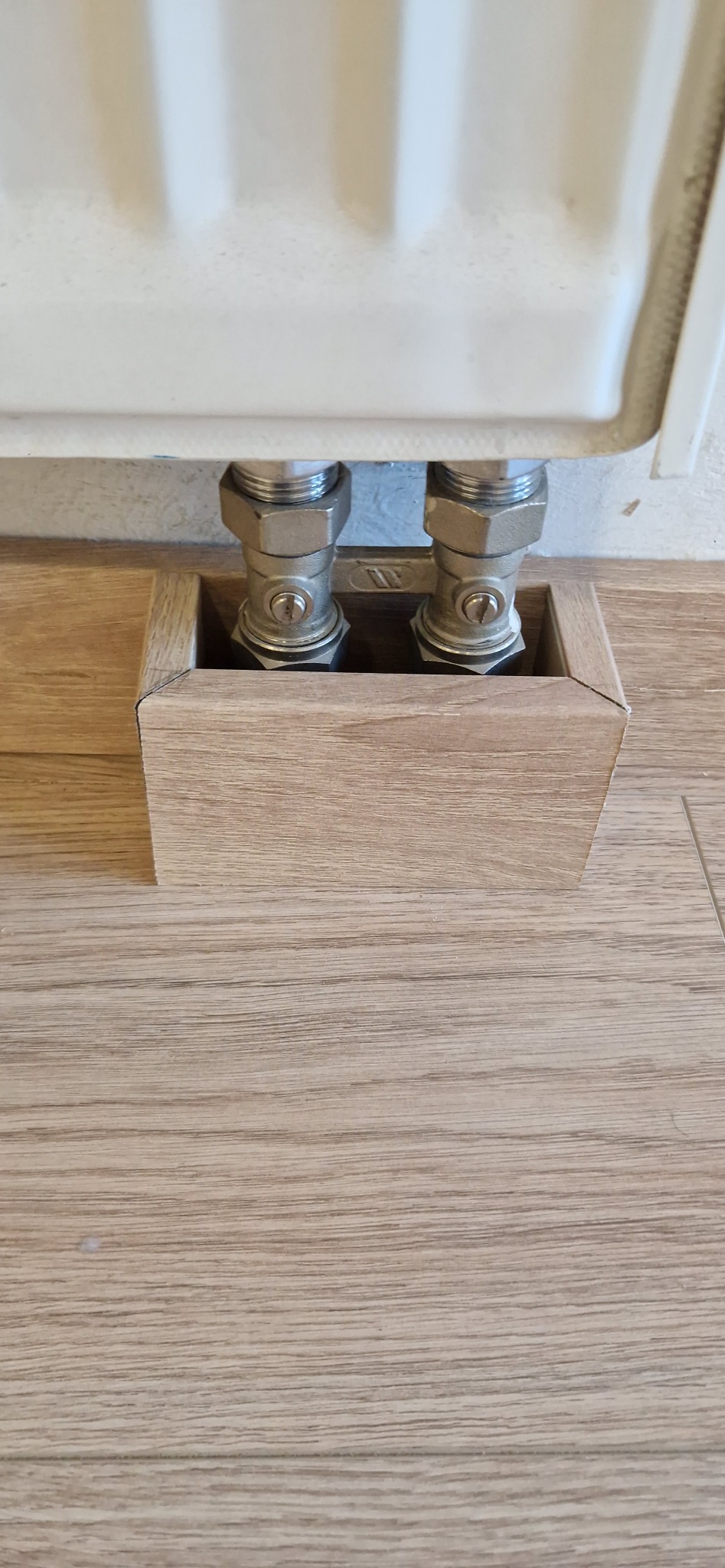 Maskownica z paneli podłogowych zakrywająca rury grzejnika, dopasowana kolorystycznie do podłogi. Estetyczne wykończenie wnętrza.