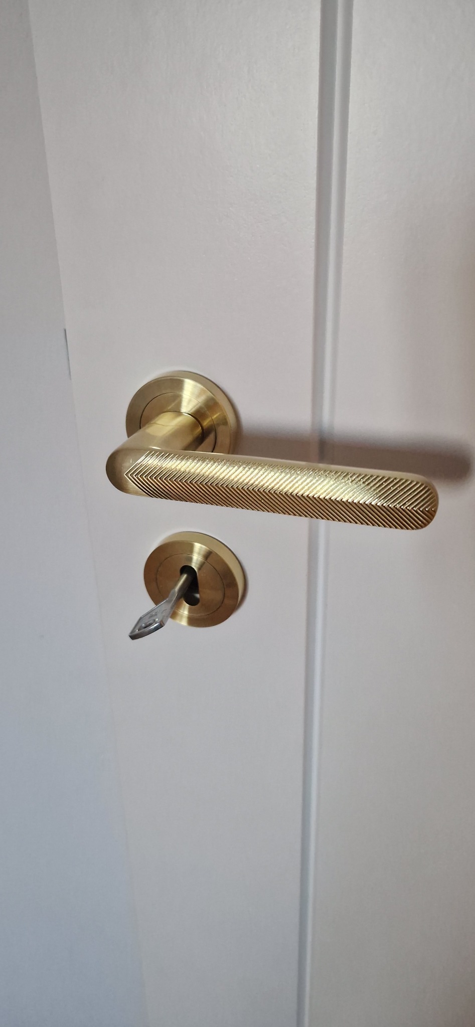 Białe drzwi z zamontowaną złotą klamką o teksturowanej powierzchni i kluczem w zamku, ukazujące dbałość o detale wykończenia wnętrza.