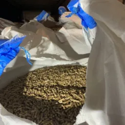 Pellet drzewny w workach typu big bag, z niebieskimi akcentami, w magazynie. Widok z g&oacute;ry na wypełniony worek z bliska. Delikatne oświetlenie.