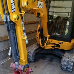 Michał - Żółto-czarna minikoparka JCB 8025 ZTS z czerwonym osprzętem roboczym, widoczna z bliska, umieszczona wewnątrz zabudowy pojazdu dostawczego.