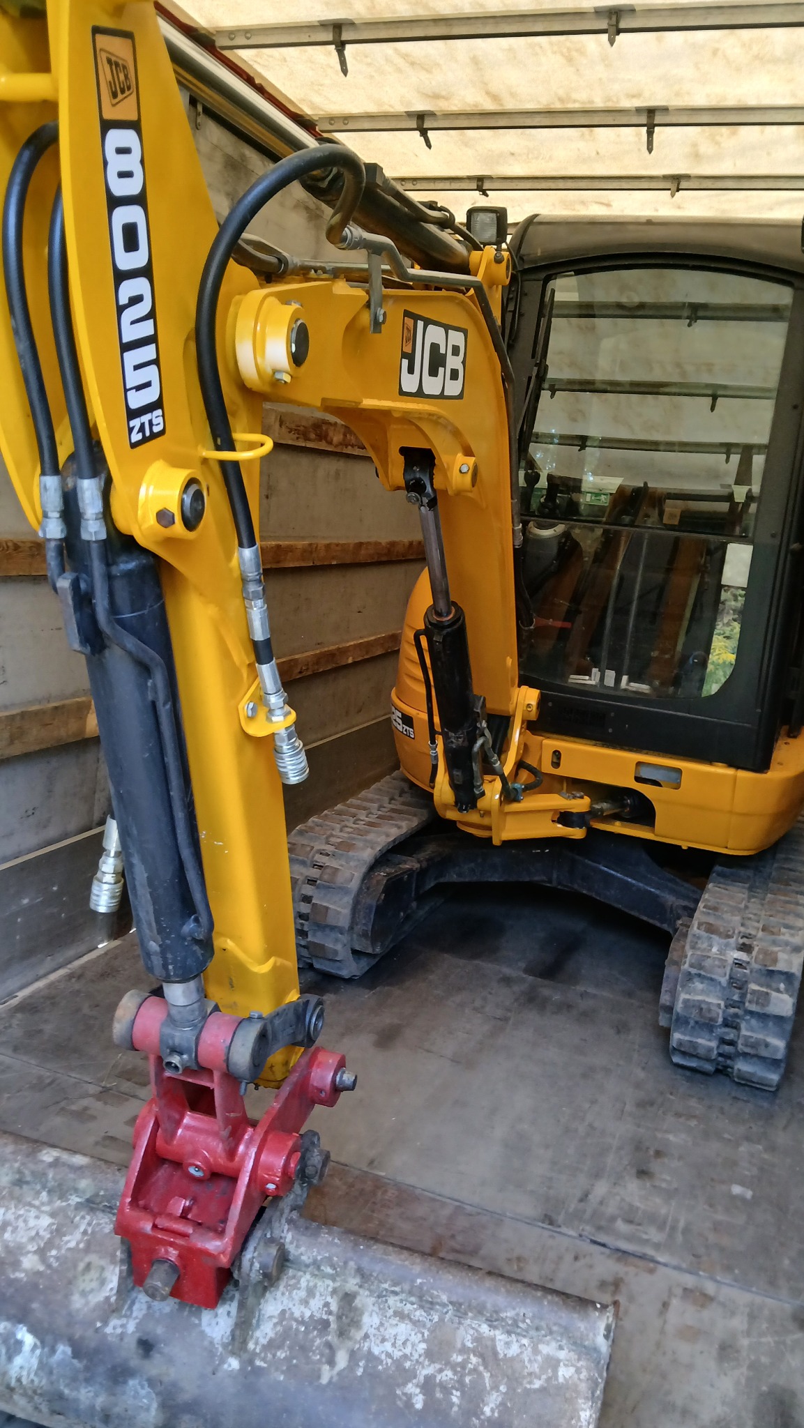 Żółto-czarna minikoparka JCB 8025 ZTS z czerwonym osprzętem roboczym, widoczna z bliska, umieszczona wewnątrz zabudowy pojazdu dostawczego.