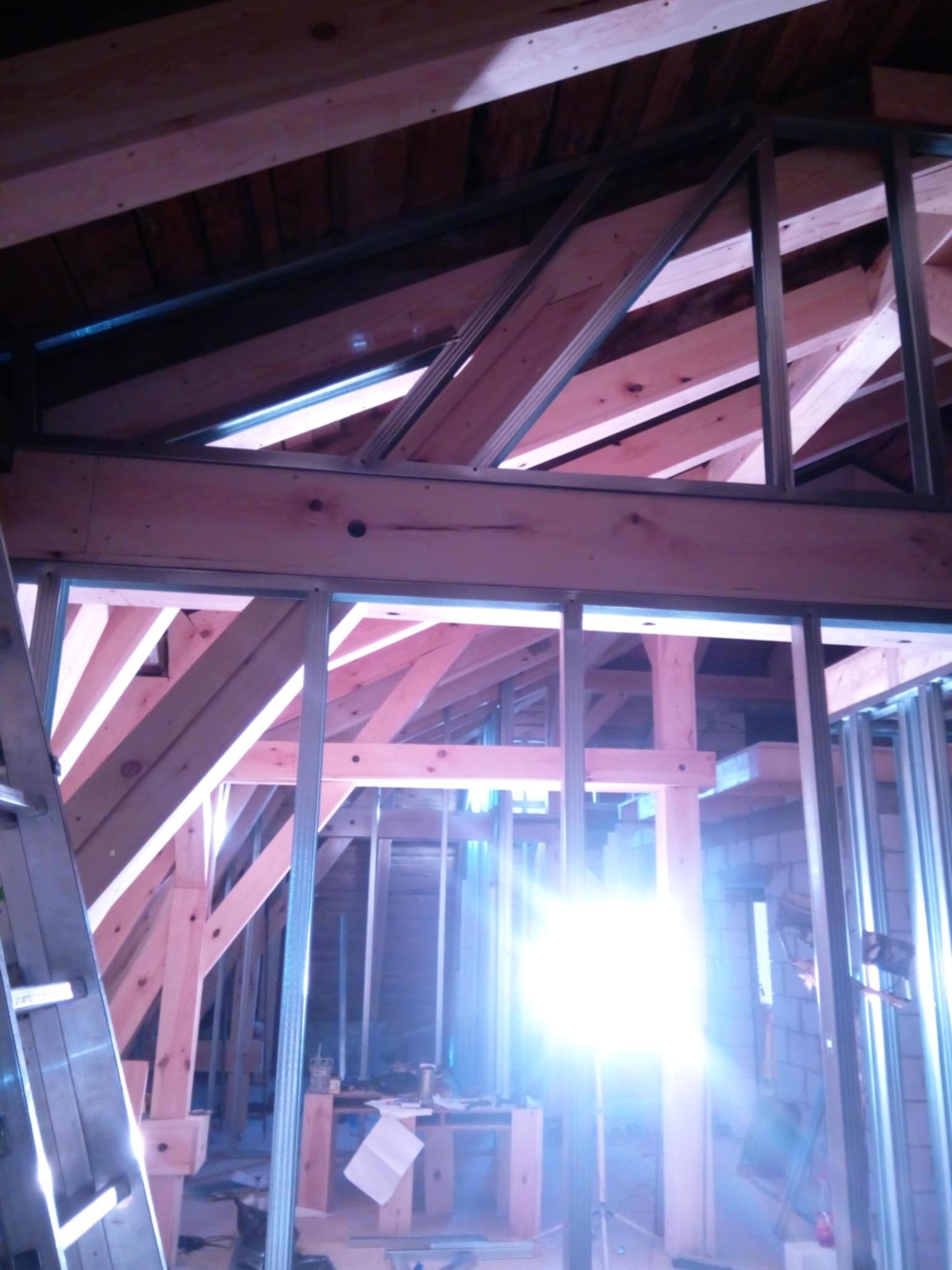 Konstrukcja poddasza z drewnianych belek i metalowych profili, widoczne elementy izolacji, oświetlenie od wewnątrz.