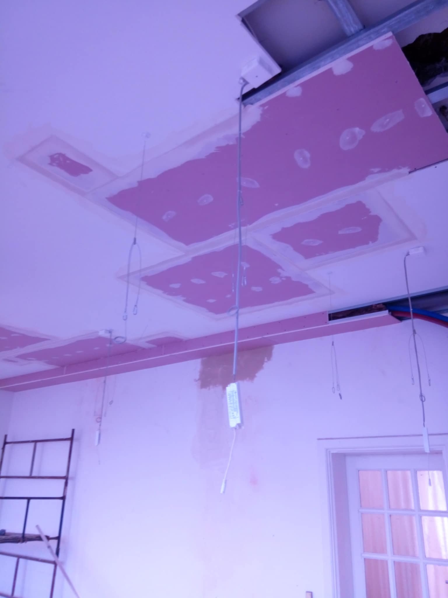 Montaż sufitu podwieszanego z płyt karton gips w pomieszczeniu z widocznymi przewodami elektrycznymi i elementami konstrukcyjnymi.