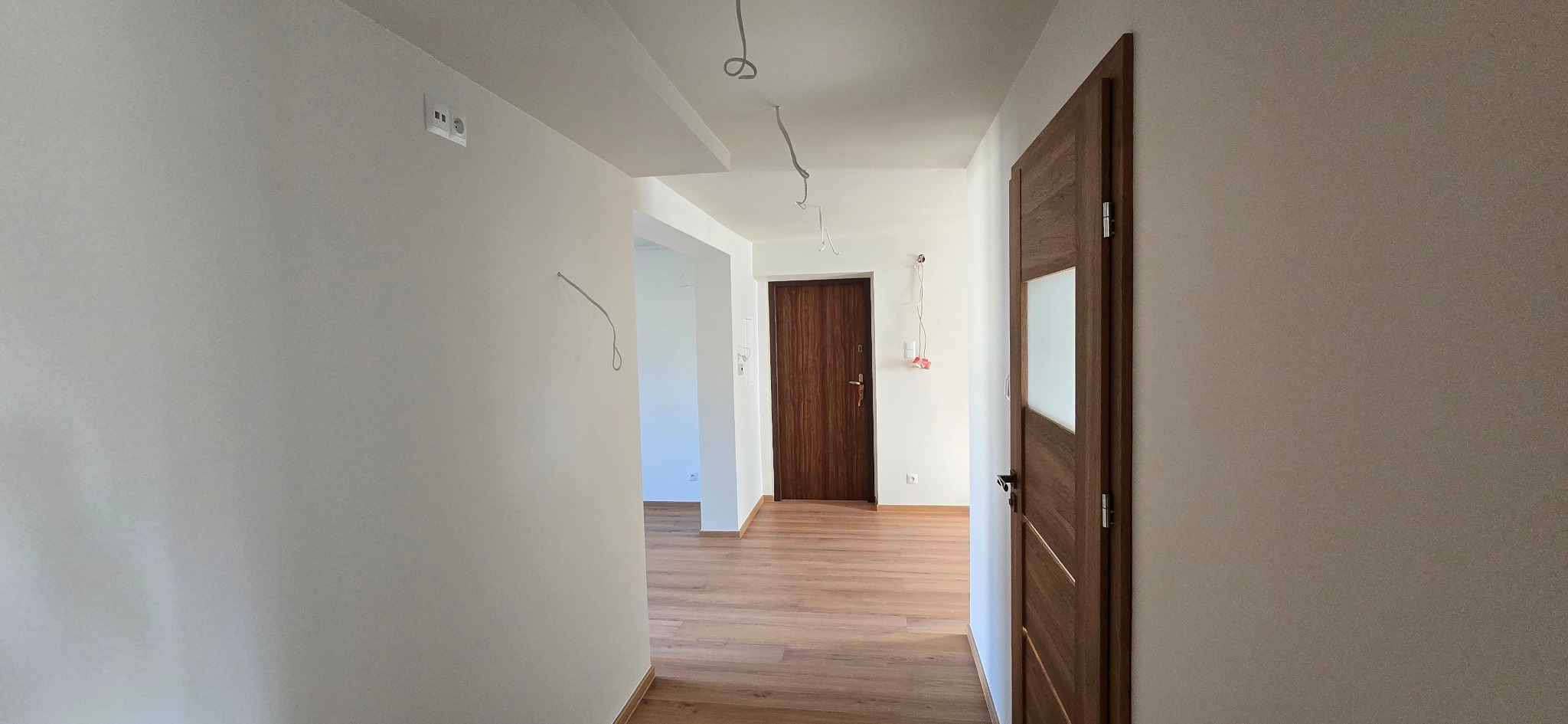 Korytarz po remoncie: świeżo pomalowane ściany w odcieniach bieli, drewnopodobne panele na podłodze i zamontowane drzwi wewnętrzne z przeszkleniem.