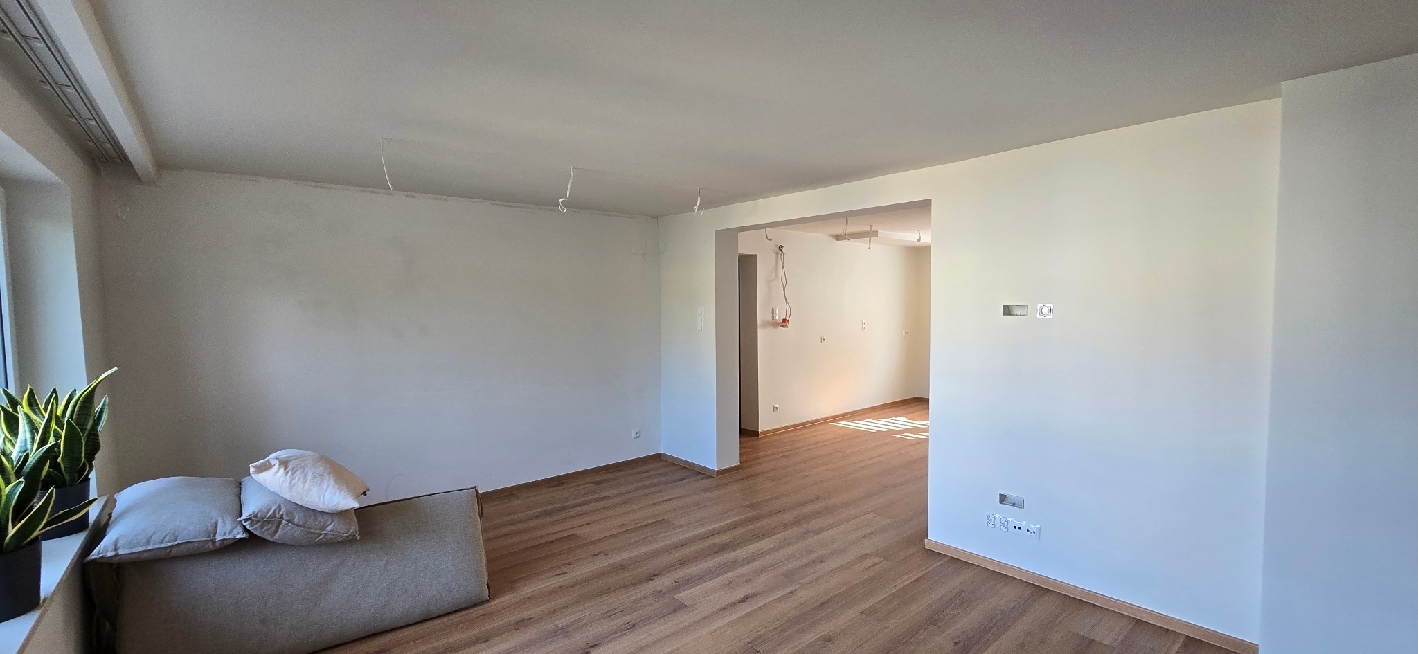 Jasne wnętrze po remoncie: świeżo pomalowane ściany, drewnopodobna podłoga, widoczne gniazdka elektryczne i przygotowane punkty oświetleniowe na suficie.