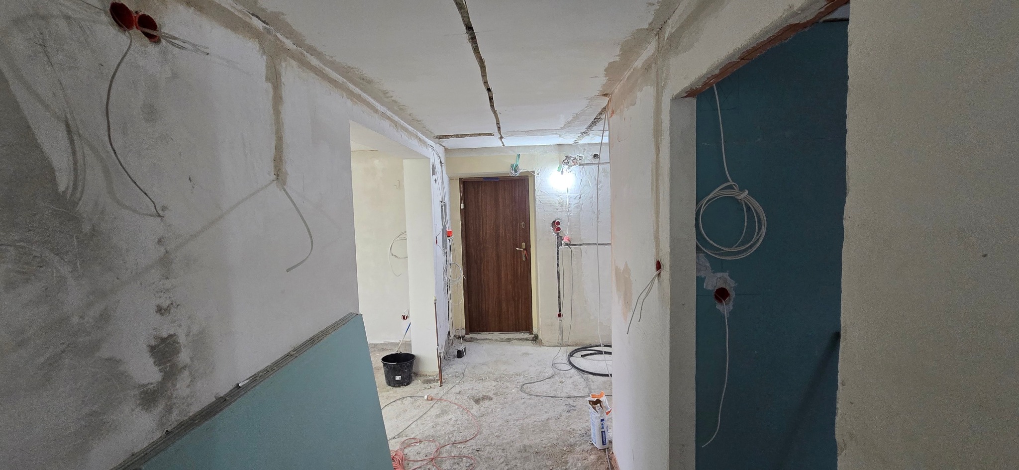 Wnętrze w trakcie prac wykończeniowych: surowe ściany, widoczne instalacje elektryczne, płyty gipsowo-kartonowe, przygotowanie do dalszych etapów prac.