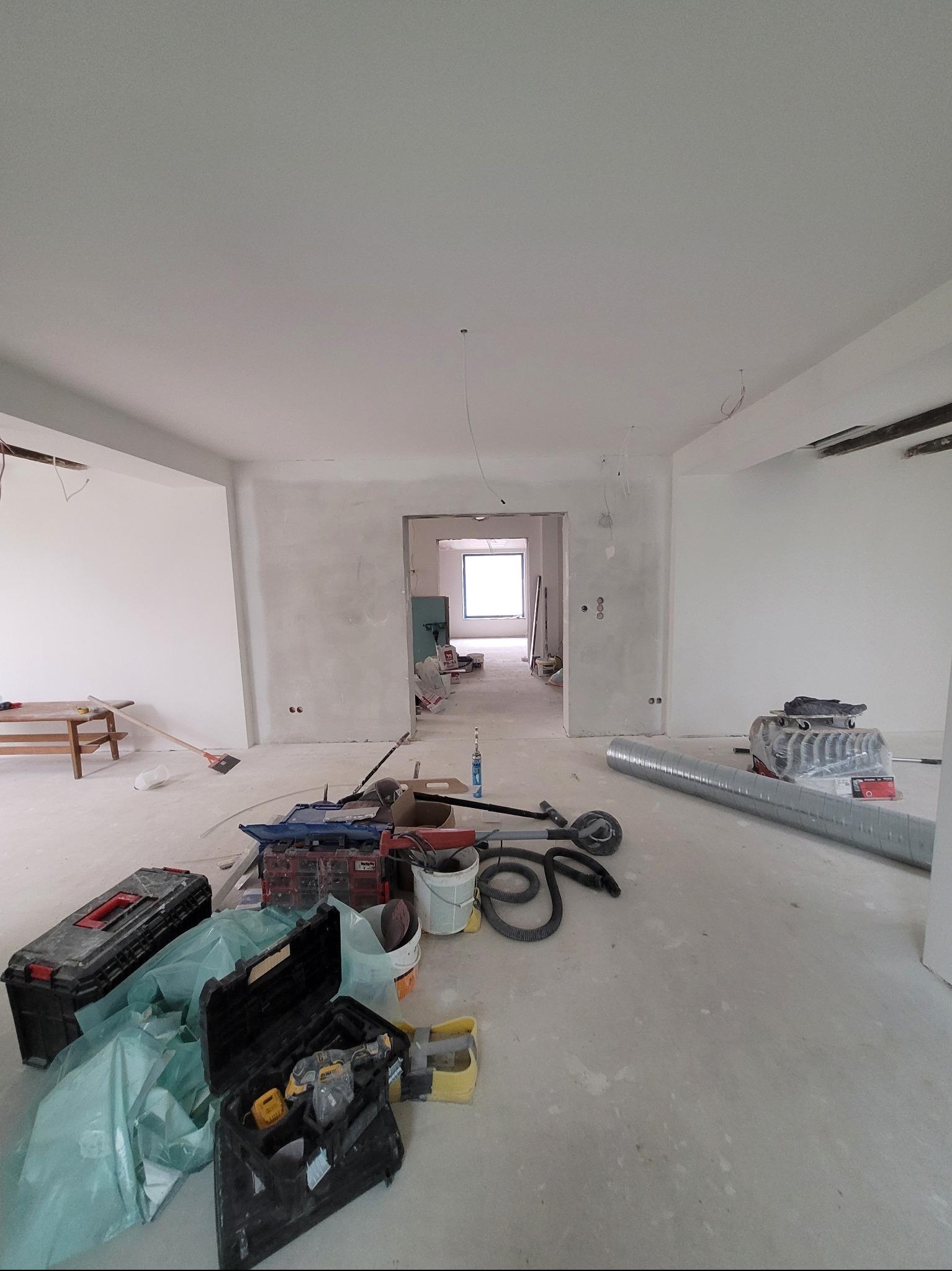 Wnętrze w trakcie prac wykończeniowych w Rzeszowie. Widoczne narzędzia, szpachlowane ściany i sufit, przygotowane do dalszych prac. Duże okno w tle.