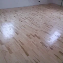 Jasna, drewniana podłoga parkietowa ułożona pod kątem w nowo wykończonym wnętrzu poddasza, widoczne kable elektryczne zwisające z sufitu.