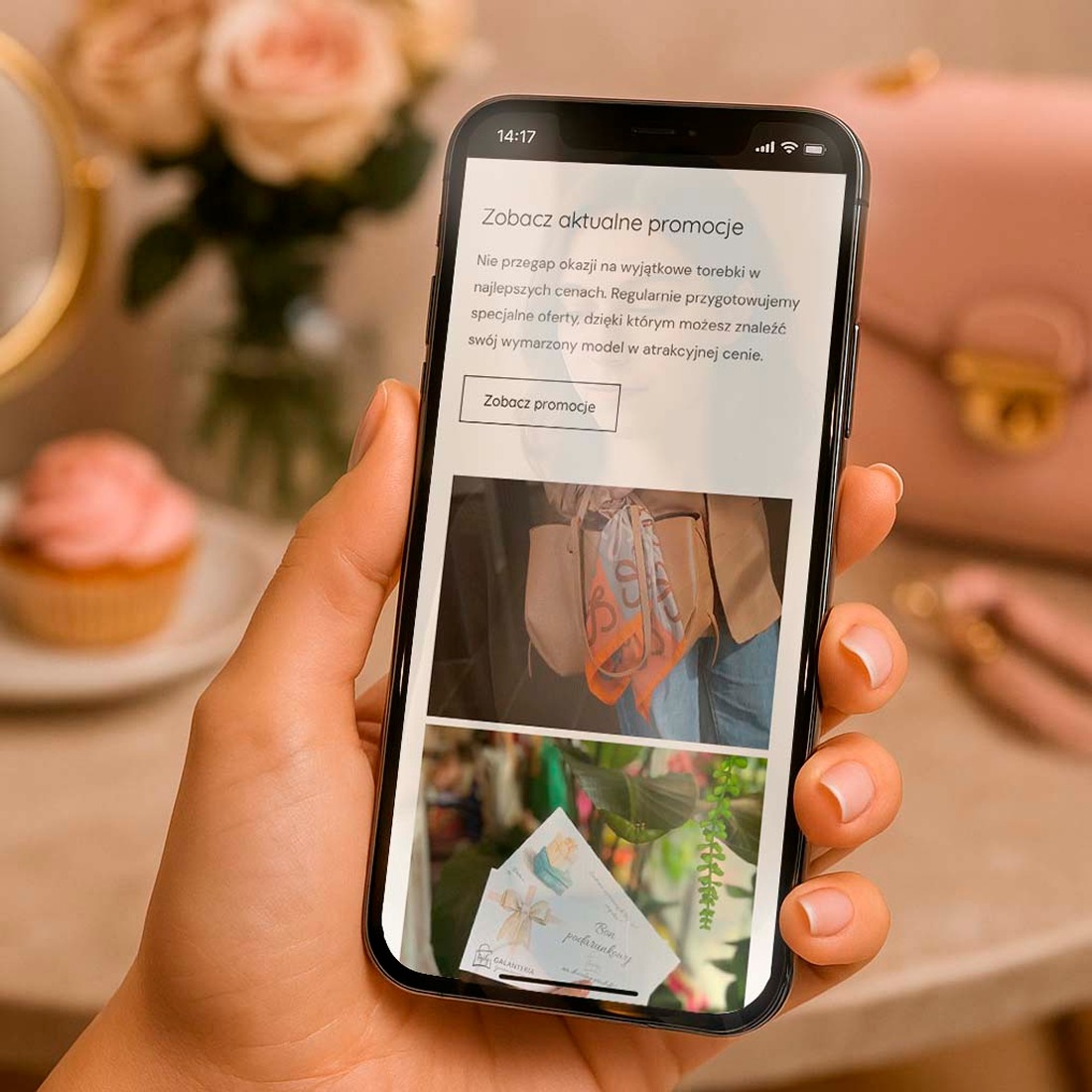 Smartfon w dłoni wyświetla stronę z promocjami na torebki, z przyciskiem 'Zobacz promocje'. W tle babeczka i kwiaty, sugerujące kobiecy charakter oferty.