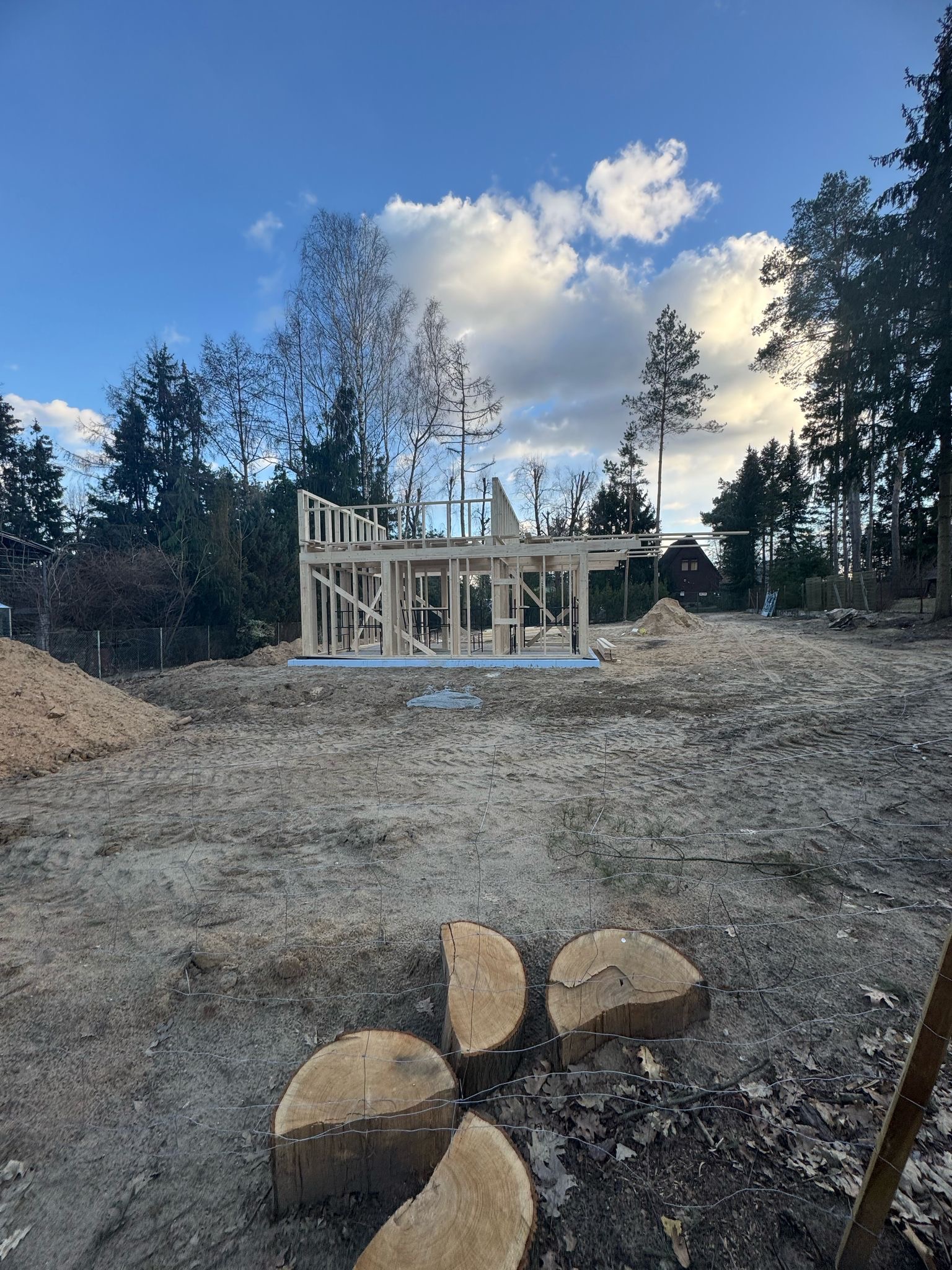 Budowa domu szkieletowego w Warszawie, widok na drewniany szkielet konstrukcji na działce, w tle drzewa i częściowo widoczny budynek.