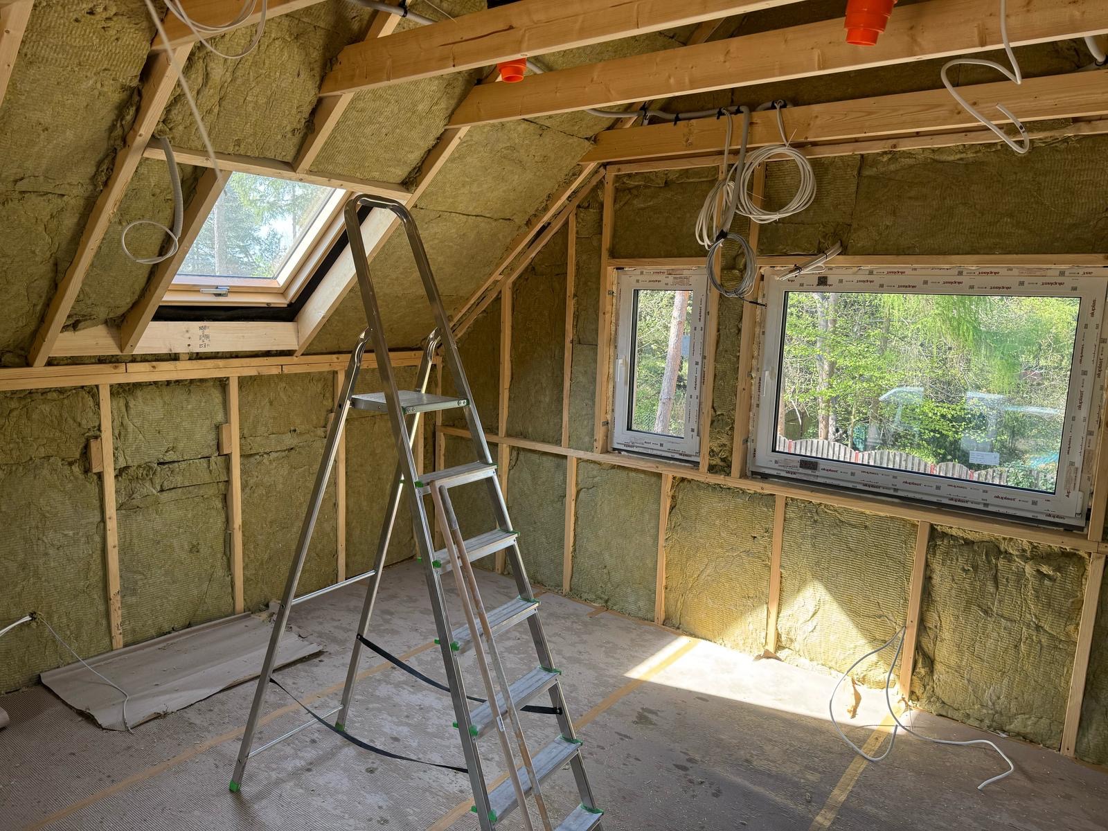 Poddasze z oknami połaciowymi i ścianami wypełnionymi izolacją z wełny mineralnej. Widoczna drabina, drewniana konstrukcja i instalacje elektryczne.