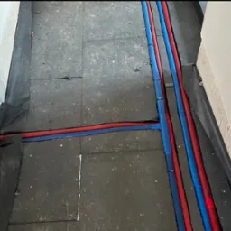Instalacja rur grzewczych (czerwone i niebieskie) na podłożu. Prace hydrauliczne w Toruniu przed wylaniem posadzki. Widok z góry, rury ułożone wzdłuż ściany.