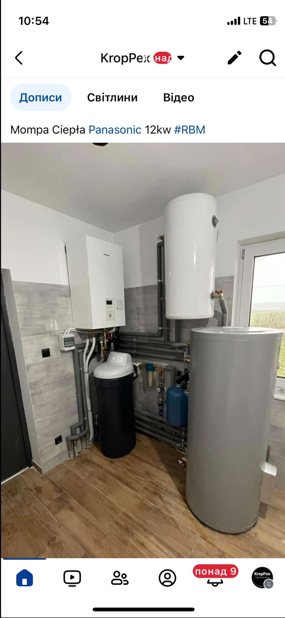 Pompa ciepła Panasonic 12kW z zbiornikami i filtrem wody w pomieszczeniu z drewnopodobną podłogą i szarą glazurą. Widoczne liczne rury i instalacje.