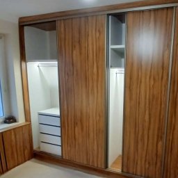 Magdalena Oniszczuk - Szafa wnękowa z przesuwnymi drzwiami o drewnianym wzorze, z widocznymi półkami i szufladami wewnątrz. Oświetlenie LED podkreśla wnętrze szafy.