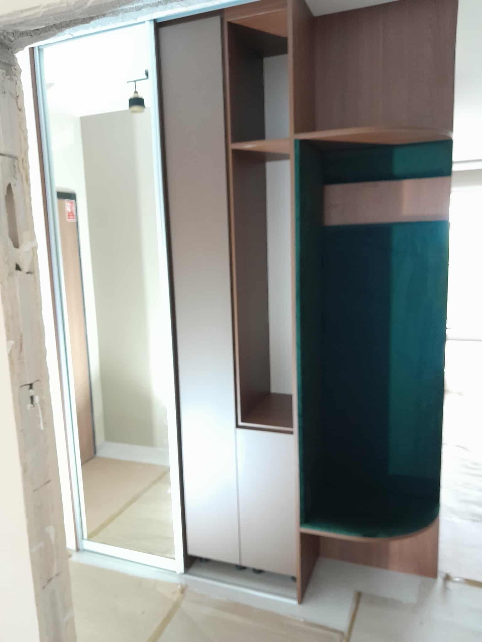 Wnętrze z szafą wnękową z przesuwnymi drzwiami i otwartymi półkami, widoczne elementy wykończeniowe, surowy stan pomieszczenia.