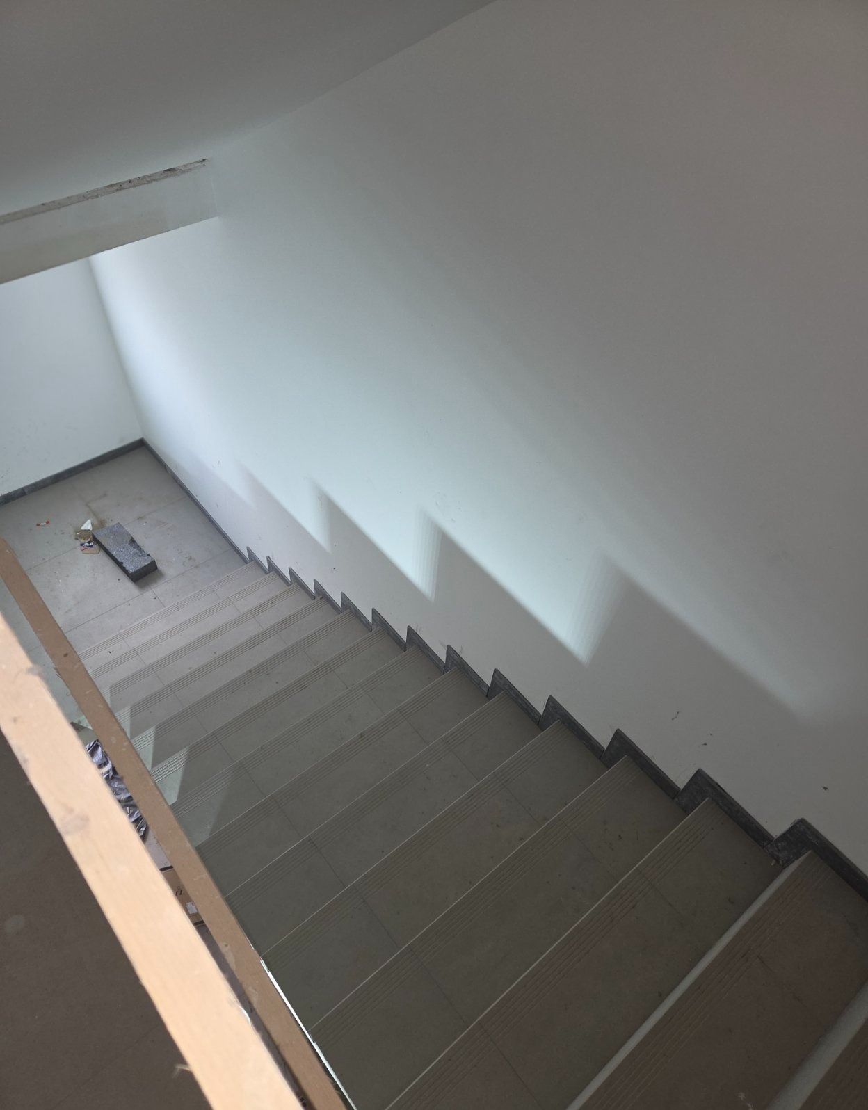 Klatka schodowa z wyłożonymi płytkami schodami, widok z góry. Widoczne świeże, białe ściany i szare płytki na schodach z ciemnymi krawędziami.