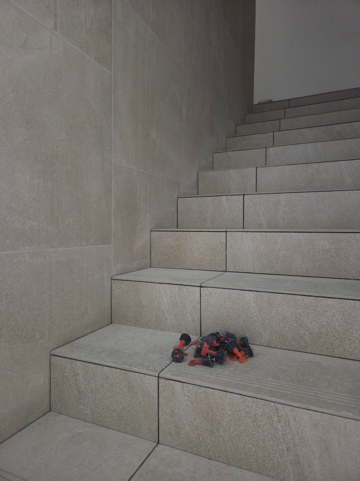 Wykończone schody z płytek w odcieniach beżu, z narzędziami do układania płytek na pierwszym planie, ukazujące precyzję wykonania.