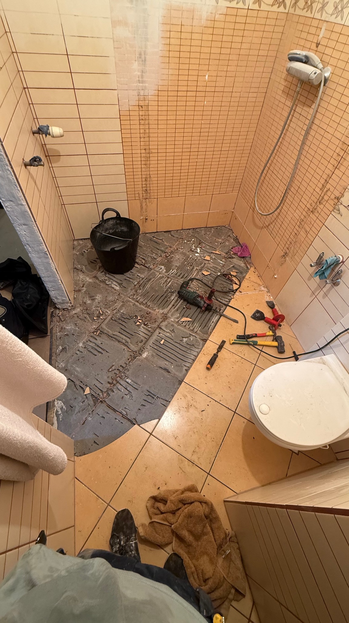 Demontaż płytek w łazience. Widoczne narzędzia, gruz i przygotowane ściany. Perspektywa z góry ukazuje etap prac przed położeniem nowych płytek.