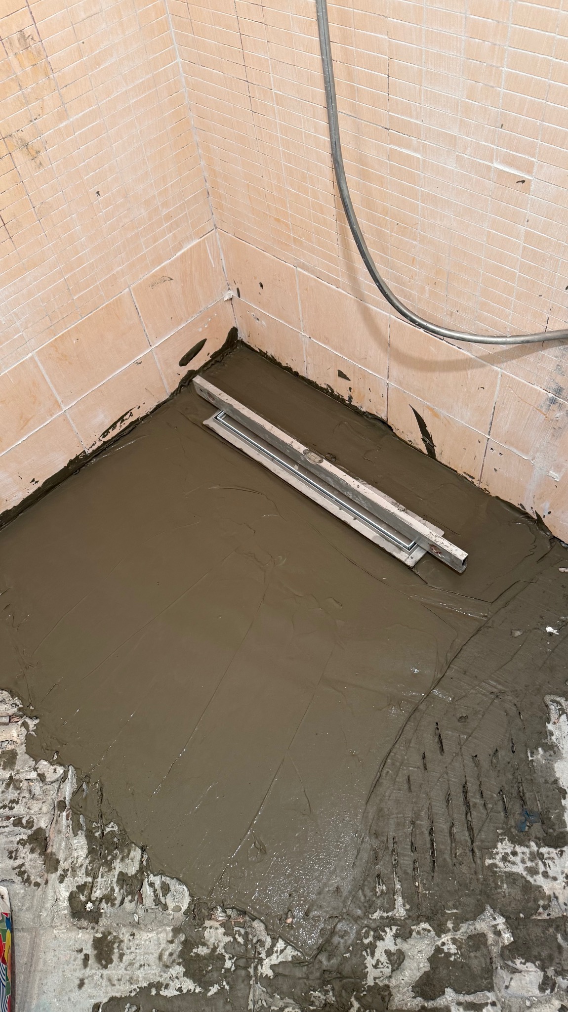 Przygotowanie podłoża pod płytki w łazience. Wyrównana wylewka z poziomnicą, ściany z jasnych płytek. Widoczne ślady po pracach remontowych.