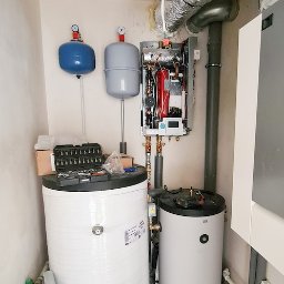 Serwis Fabryczny Urządzeń Gazowo-Elektrycznych - Szymaniak - oddział Szczecin - Kotłownia z dwoma zbiornikami, piecem gazowym, narzędziami i elementami instalacji grzewczej w pomieszczeniu. Widoczne rury, zawory i inne komponenty.
