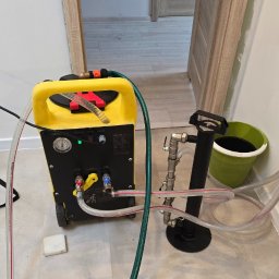 Serwis Fabryczny Urządzeń Gazowo-Elektrycznych - Szymaniak - oddział Szczecin - Żółte urządzenie do przepychania rur podłączone do instalacji, z widocznymi przewodami i manometrem, w pomieszczeniu z otwartymi drzwiami w tle.