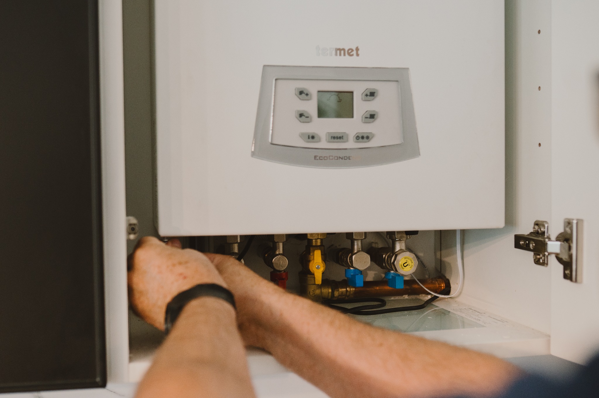 Instalacja pieca gazowego Termet EcoCondens Gold Plus w szafce. Widoczne zawory i podłączenia. Ręce montera przy pracy, szafka w jasnej kolorystyce.