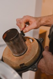 Czyszczenie palnika gazowego kotła z osadów. Widoczne dłonie serwisanta, palnik z siatką i osad. Ujęcie z bliska, oświetlenie naturalne.