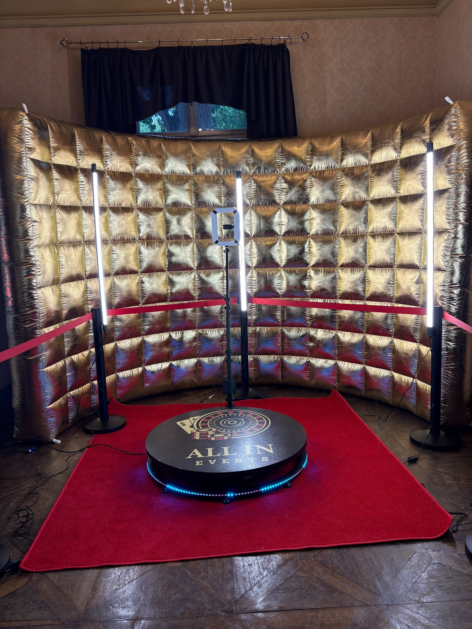 Złota ścianka i platforma obrotowa ze światłami LED na czerwonym dywanie, tworzące wystawne tło do zdjęć.