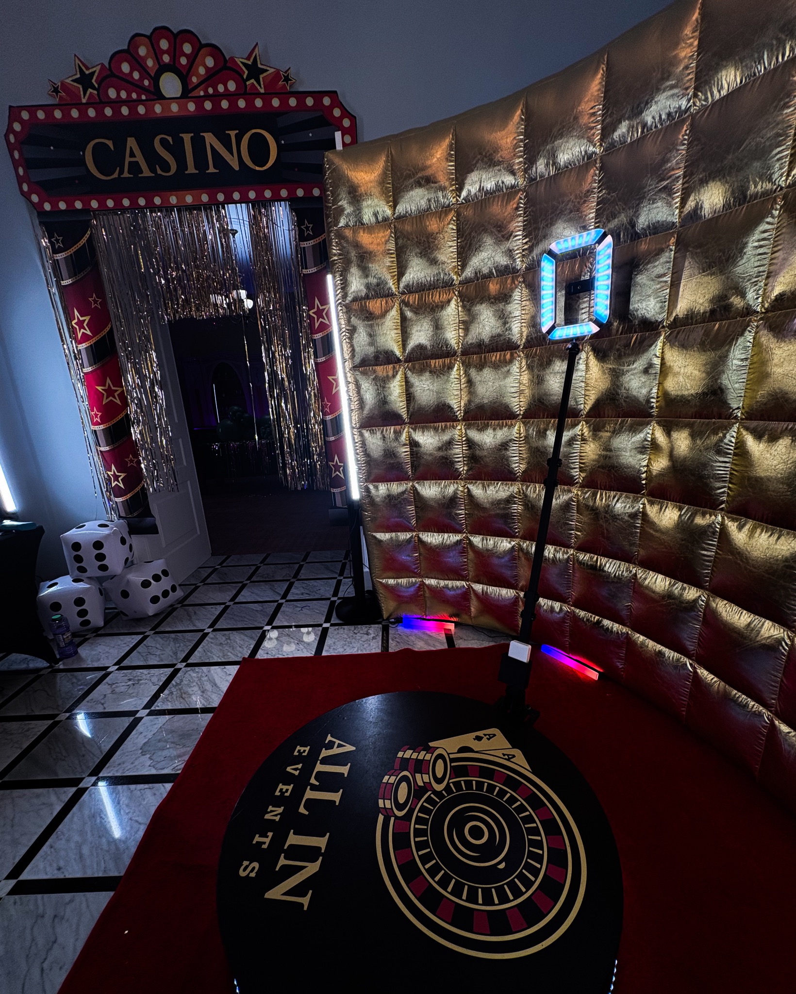 Tematyczna aranżacja imprezowa w stylu kasyna: złota ściana, dekoracyjny napis 'Casino', kostki do gry i okrągła platforma z motywem ruletki.