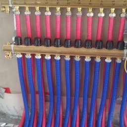 MSB-INSTAL - Rozdzielacz ogrzewania podłogowego z rurami w kolorach niebieskim i czerwonym. Widoczne oznaczenia numeryczne na rozdzielaczu. Instalacja w trakcie montażu.