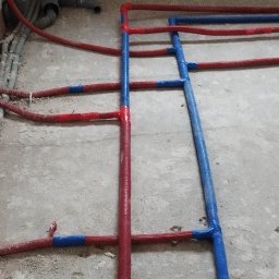 MSB-INSTAL - Instalacja grzewcza podłogowa w trakcie montażu, rury w izolacji czerwonej i niebieskiej, widoczne złącza i mocowania na surowym podłożu.