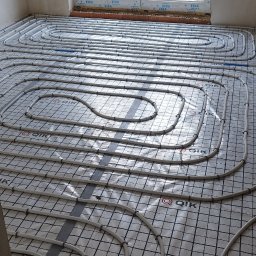 MSB-INSTAL - Białe rury ogrzewania podłogowego ułożone na folii z nadrukiem QIK, widoczne przez okno drzewa.