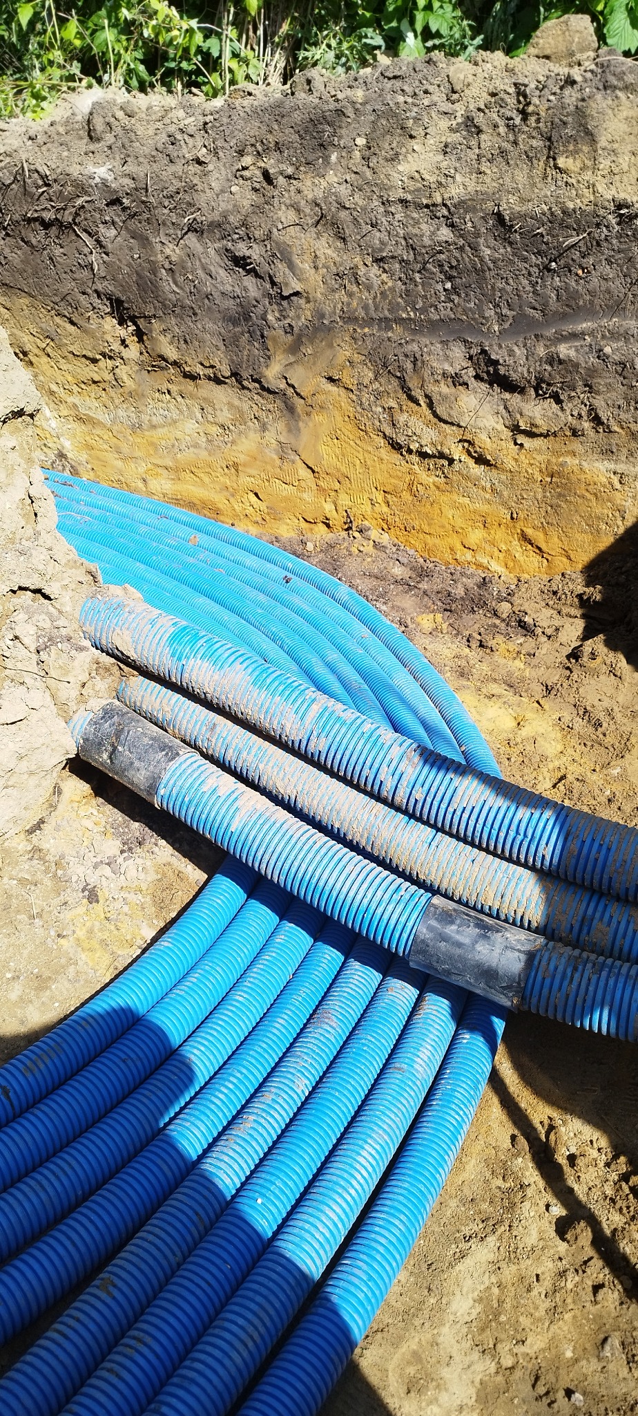 Niebieskie rury karbowane ułożone w wykopie ziemnym, częściowo zasypane piaskiem. Widoczne złącza rur. Instalacja w ziemi.
