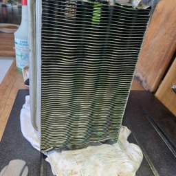 Metgen Service Krzysztof Rekus - Wymiennik ciepła z pieca gazowego, widoczne ślady użytkowania i czyszczenia. Element leży na ściereczce, w tle butelka środka czyszczącego i fragment blatu.