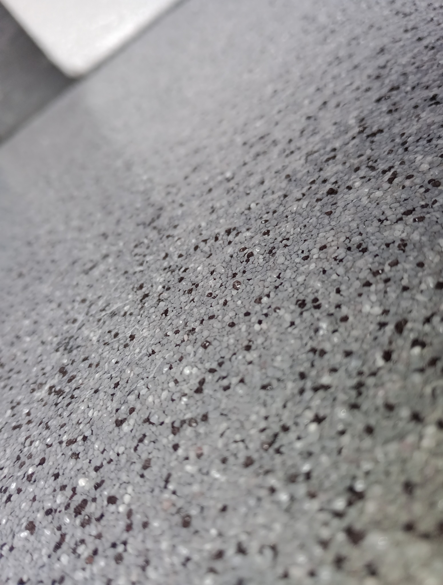 Szara posadzka żywiczna z czarnymi drobinkami, wykonana pod kątem. Gładka powierzchnia, bliski kadr.