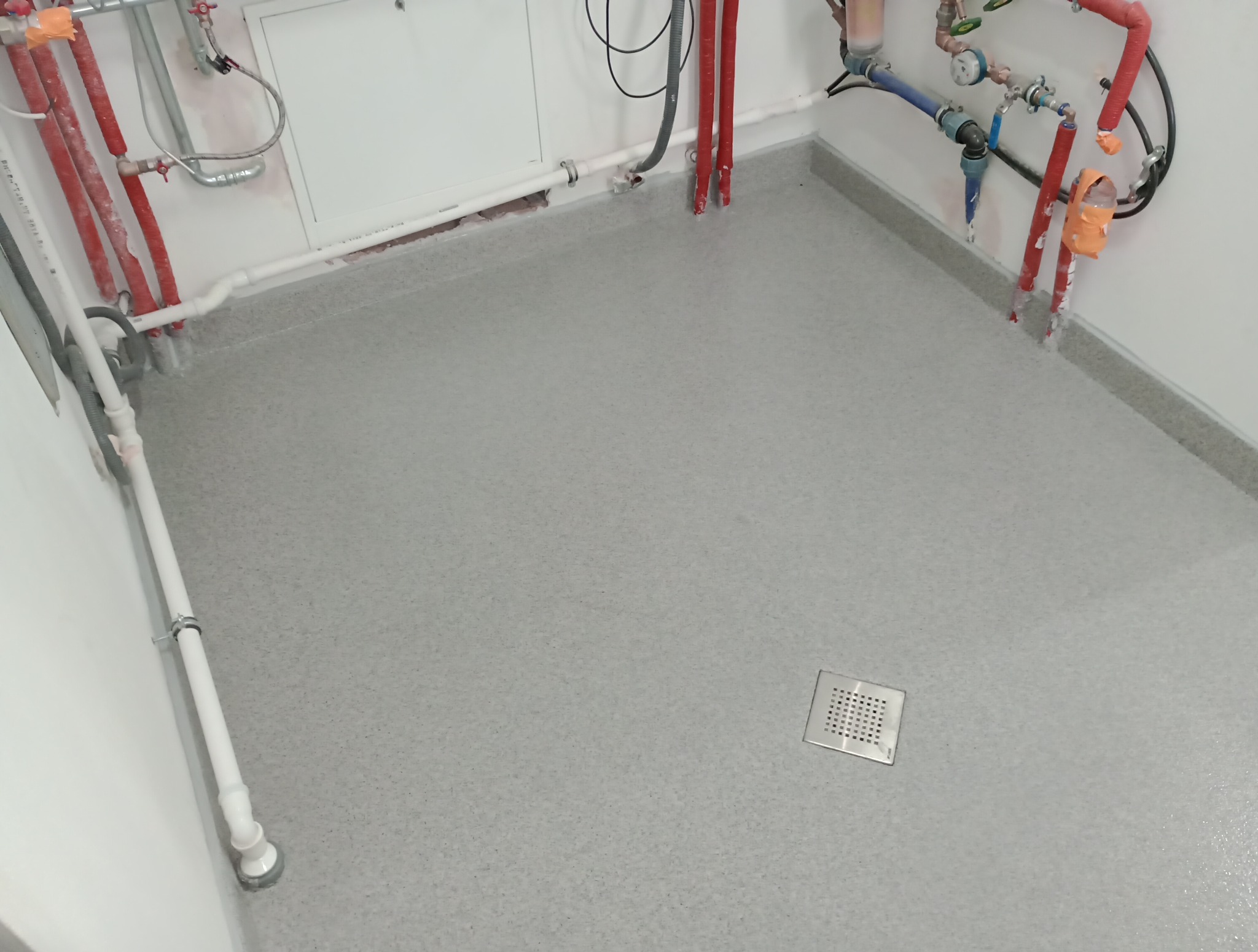 Szara posadzka żywiczna z odpływem liniowym w pomieszczeniu technicznym, Dąbrowa Tarnowska. Widoczne rury instalacyjne przy ścianach.