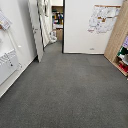 CosmoClean - Szary dywan w biurze po praniu ekstrakcyjnym. Widoczny sprzęt do prania i różnica w odcieniu dywanu po zabiegu, sugerująca usunięcie zabrudzeń.