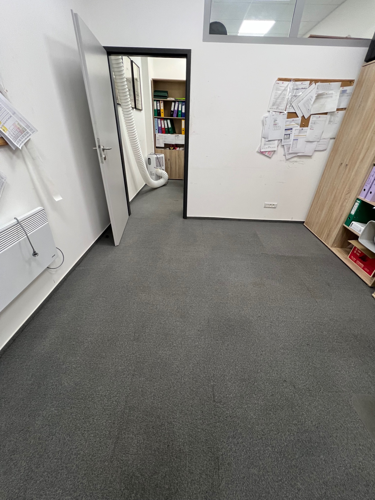 Szary dywan w biurze po praniu ekstrakcyjnym. Widoczny sprzęt do prania i różnica w odcieniu dywanu po zabiegu, sugerująca usunięcie zabrudzeń.